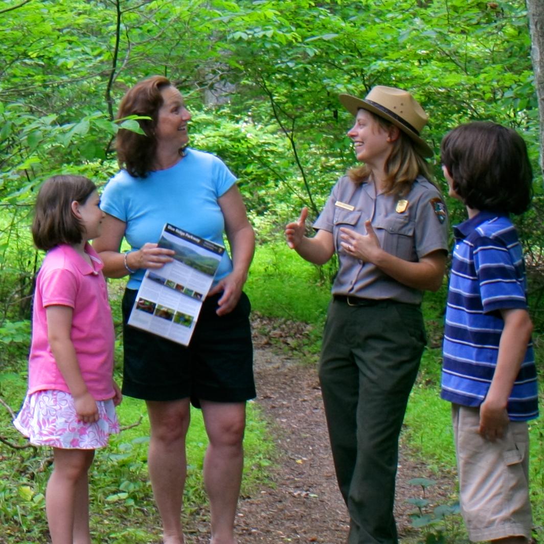 A Park Ranger is talking to a family of three on a trail in a green lush forest