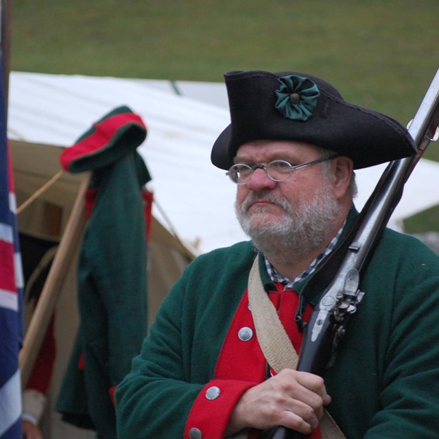 A man in Revolutionary War Era clothing holds a rifle over his shoulder.