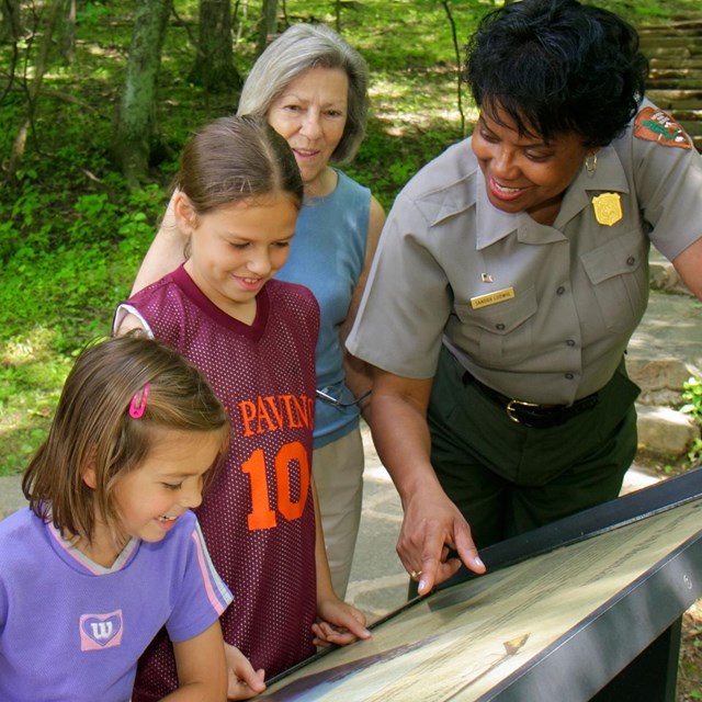 A ranger explains an exhibit panel to four visitors