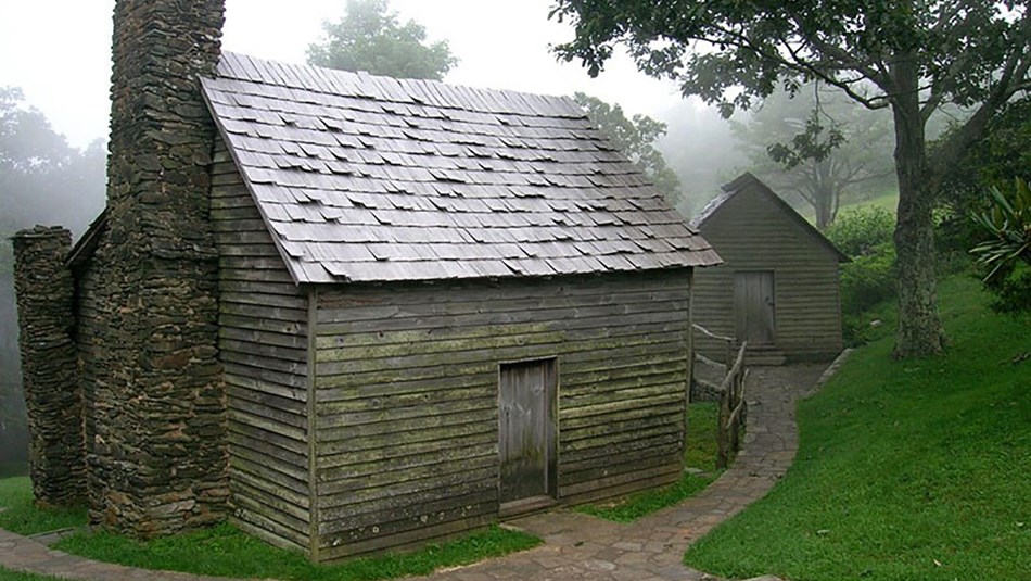 Cabin with stone chimney and walkways amongst trees; foggy