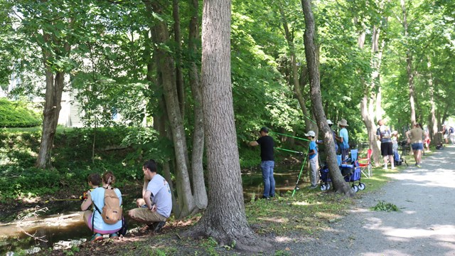Group of people standing and sitting along canal fishing