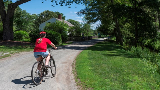 Person riding bike along stone bike path with Kelly House in background
