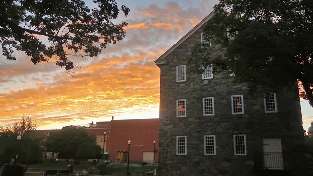 Photo of Wilkinson Mill with sunset in background behind brick building