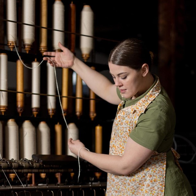 Young woman wearing green dress hold piece of cotton thread in hand in front of a machine