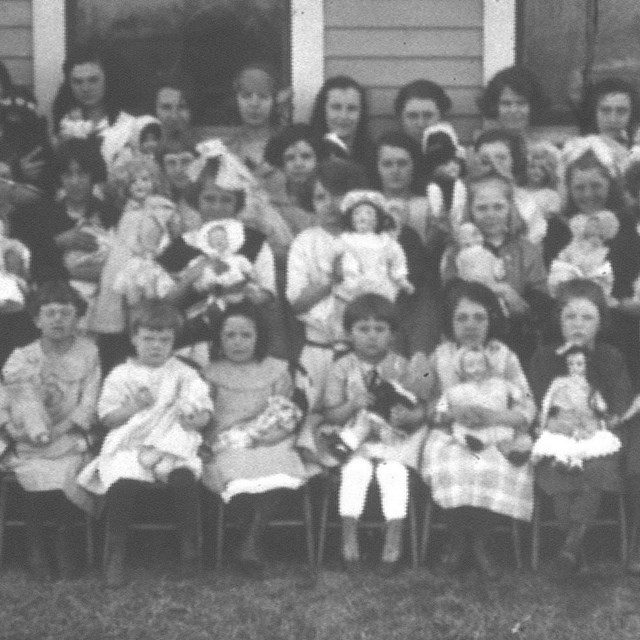 Group of young children in front of building holding dolls