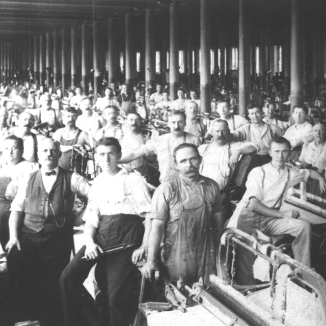 Group of men standing around looms