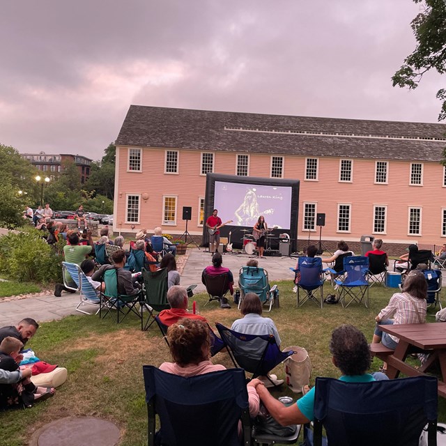 Park visitors watch a musical performance in the shadow of Slater Mill