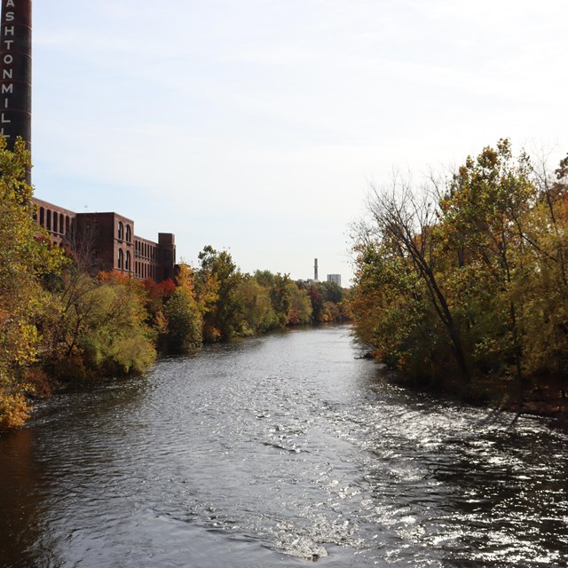 Photo of the Blackstone River with Ashton Mill on left and surrounded by trees