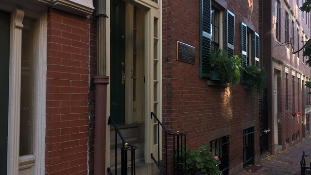 Diagonal view of shaded street of Beacon Hill with townhouses and a partial view of the sidewalk.