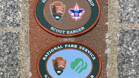 Two oval shaped scout ranger patches lined on top of the red brick of the Freedom Trail.