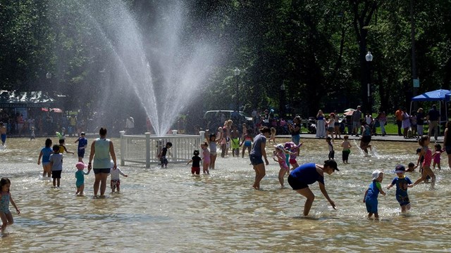 kids and adults in a shallow person-made pond with a sprinkler.