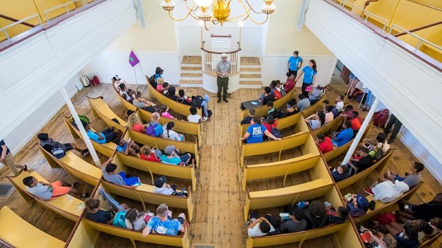 2nd floor view in African Meeting House looking onto students seated in pews with ranger speaking