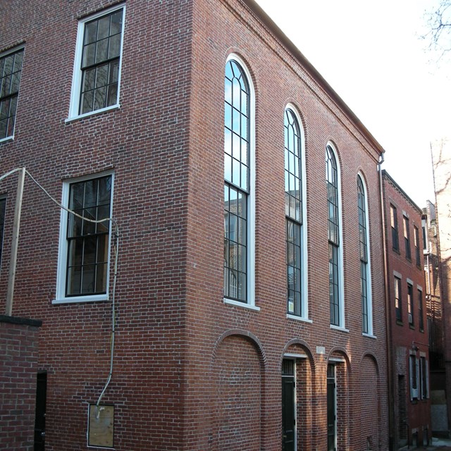 three story brick building with large arched windows from the second to third stories.