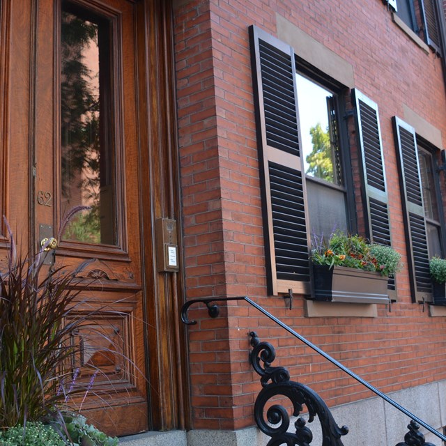 side view of a brick townhouse with a wooden ornamental door and two windows.