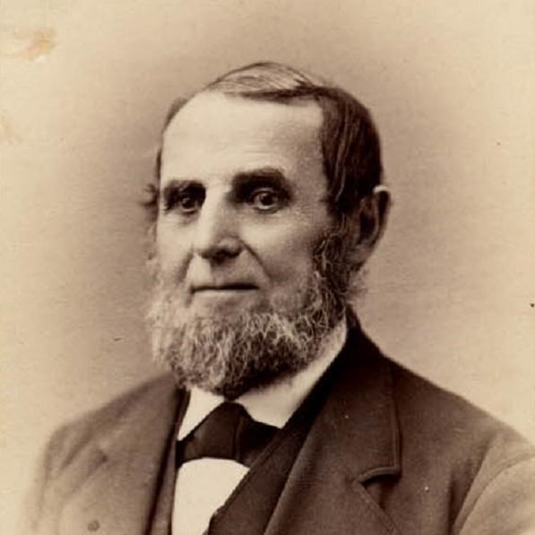 White man with a graying beard and a dark three-piece suit.  