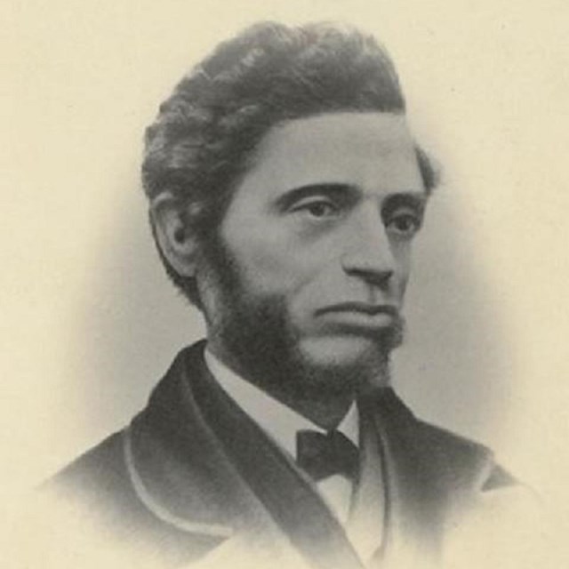 A side portrait of Nell, an African American man, with short wavy hair and side burns and a beard. 
