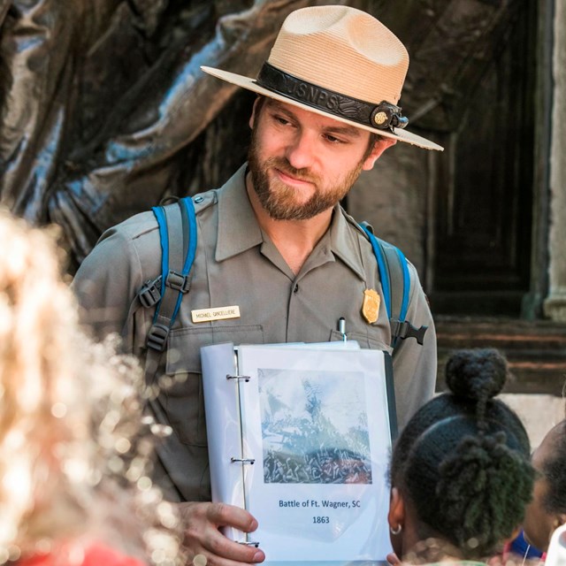 A male park ranger holds an image out for a group of students to look at.