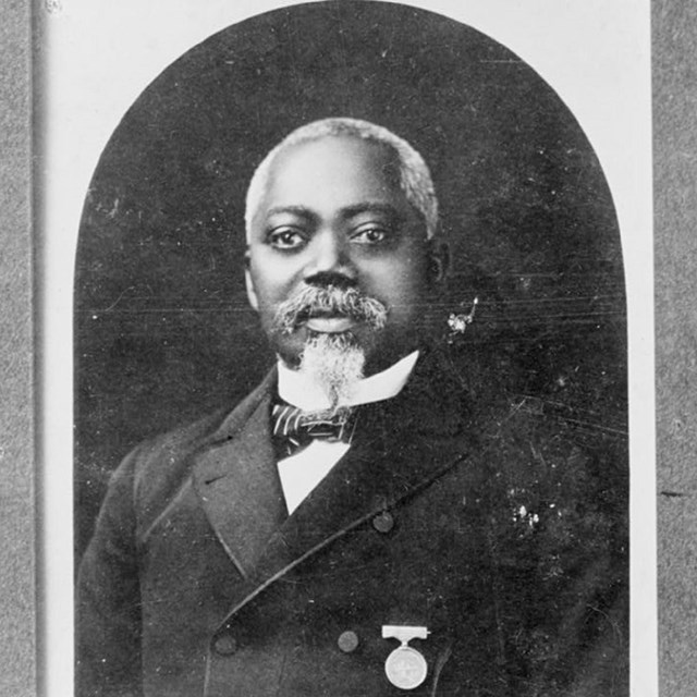 Portrait of William Carney with white balding hair and goatee wearing medal of honor on his coat.