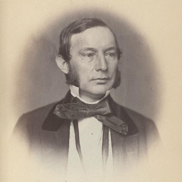 Portrait engraving of a white man with sideburns wearing a dark coat with a large bowtie.