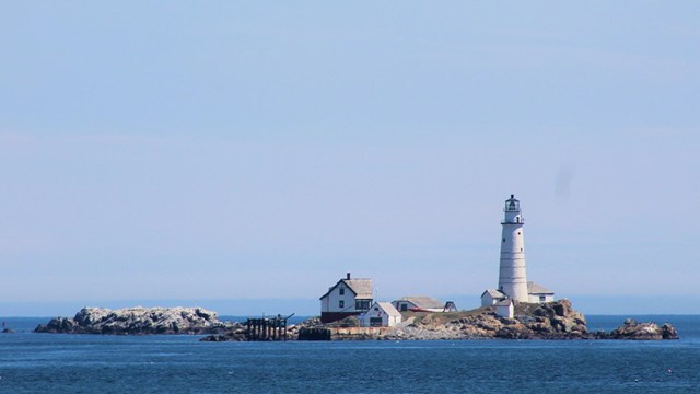 A small, rocky island with a lighthouse station, lighthouse, and other small white buildings.