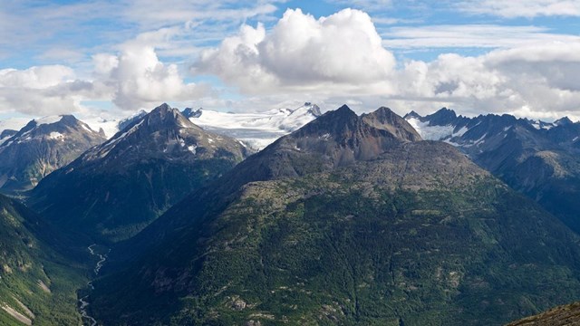 A mountain range that transitions from lush green slopes to white-capped summits.