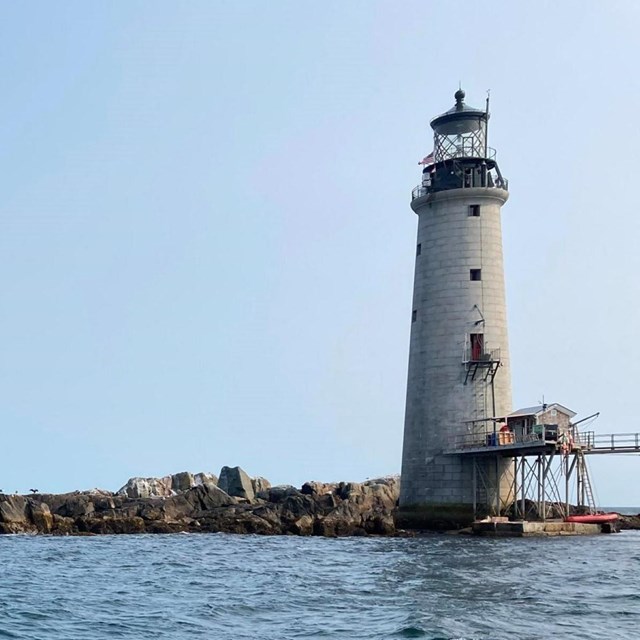 View of the rocky island looking up from the water with the grey lighthouse on the right