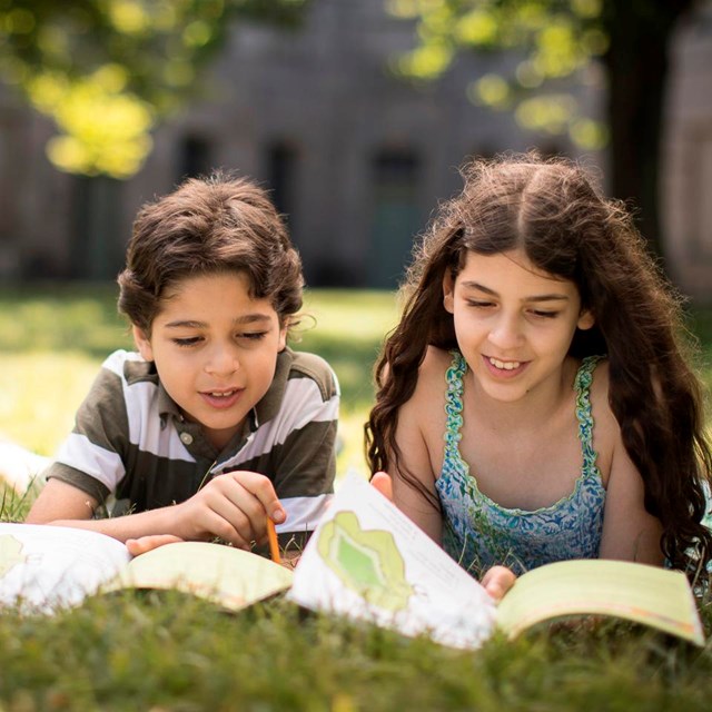 Two children laying in the grass work on Junior Ranger books.