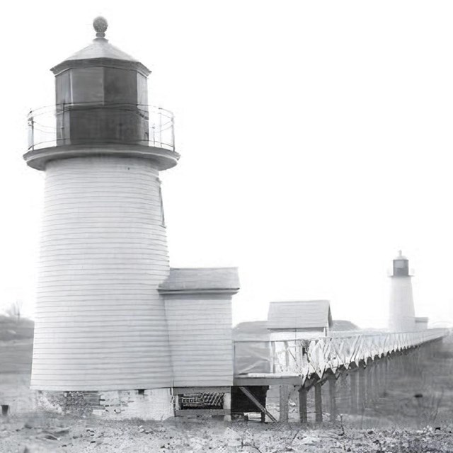 Black and white photo of a light station on a rocky beach. 