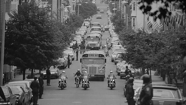 black and white photograph of a school bus being escorted by motorcycle police