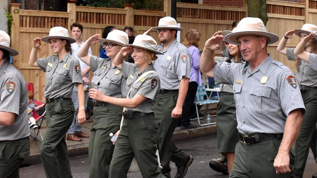Rows of uniformed NPS rangers marching and saluting.