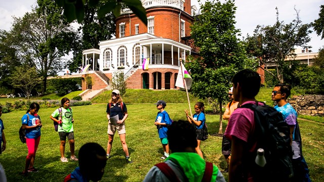 circle of kids and education team member on grassy lawn in front of commandant's house.