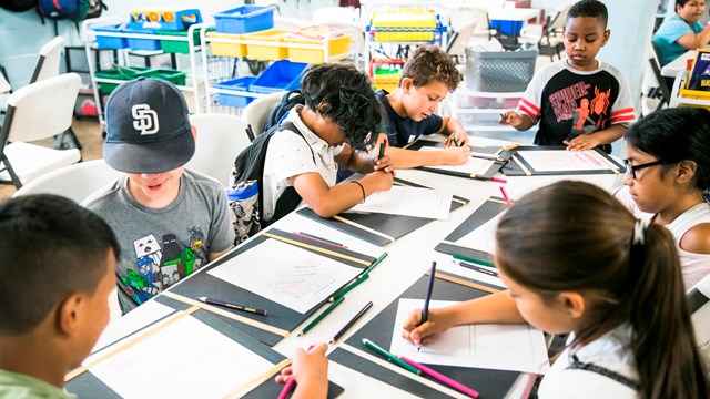 group of students sitting around a table drawing and writing.