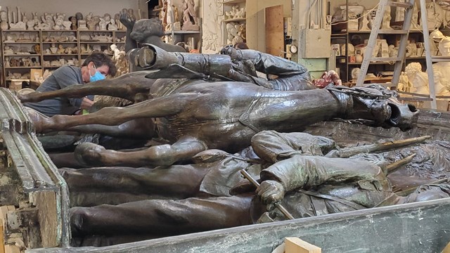 The memorial on its side with restorers working on it. 