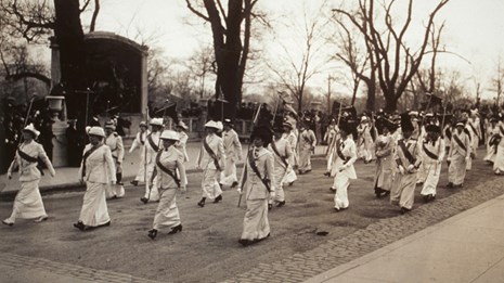 Women marching in white dresses in front of the Robert Gould Shaw 54th Memorial, Boston, MA 1914