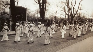 Women marching in white dresses in front of the Robert Gould Shaw 54th Memorial, Boston, MA 1914