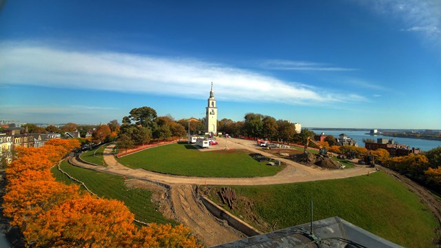 Photograph of blue sky and green grass with a white marble monument in middle.