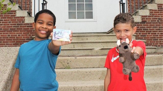 Two kids standing side-by-side, one holds up a pass card, another has a stuffed bison.