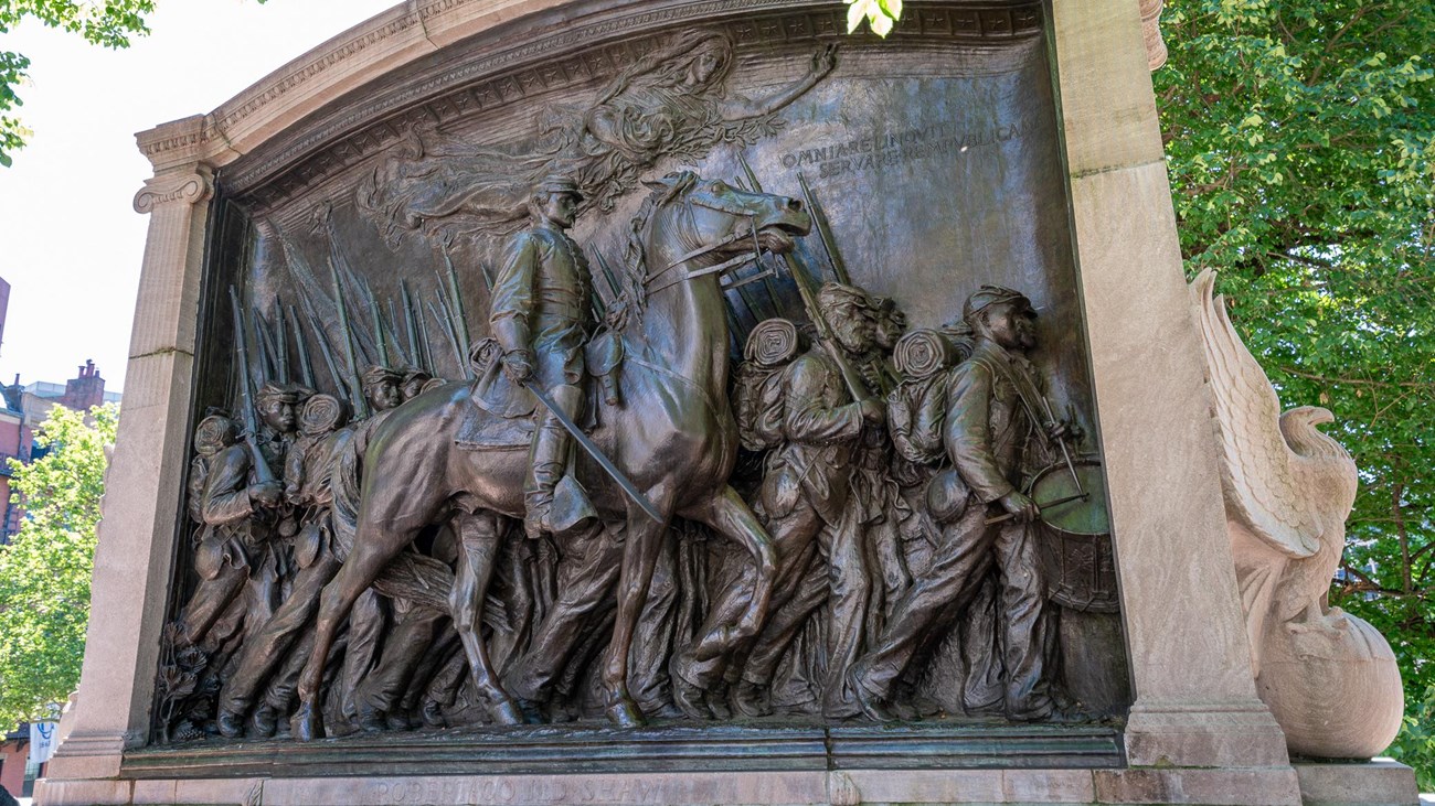 A bronze monument with a colonel on a horse with men marching in line below 
