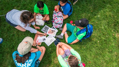 A group of kids sitting on the grass looking at print-outs of World War II posters and articles. 
