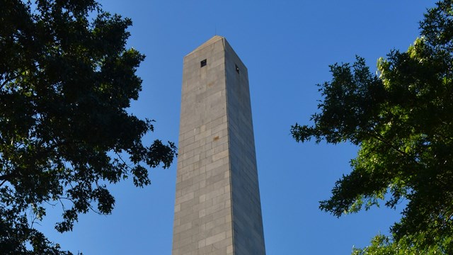 A crowd gathers on the lawn in front of the tall Bunker Hill Monument