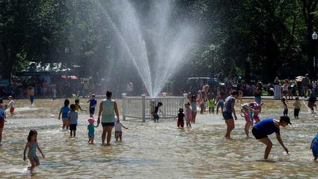 group of people enjoying a shallow human-made pond with a fountain.