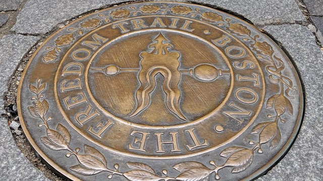 A circular bronze plaque reading "The Freedom Trail" points visitors to the red lined path.