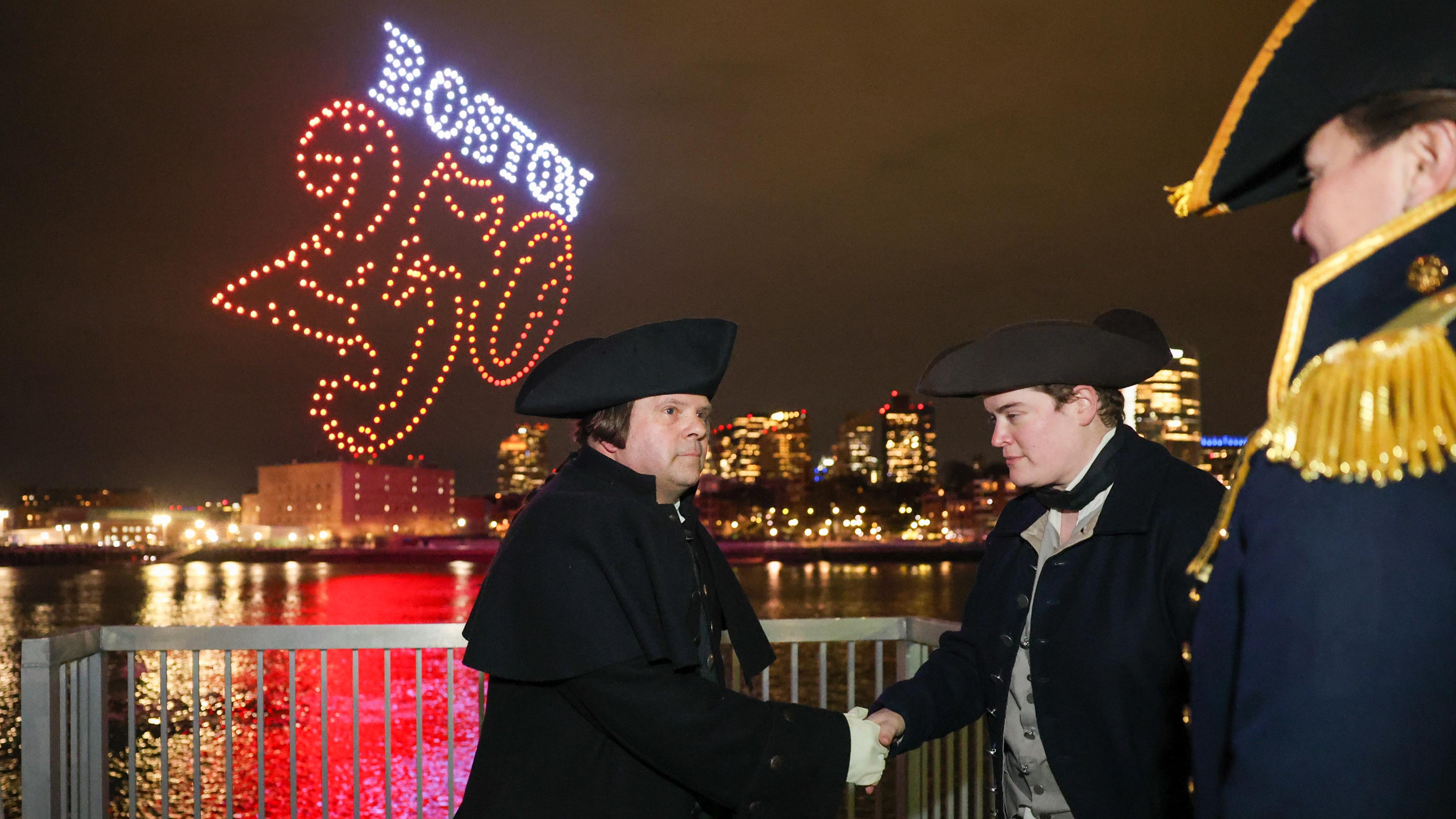 A man as Paul Revere shakes hands with a reenactor and USS Constitution Commander.