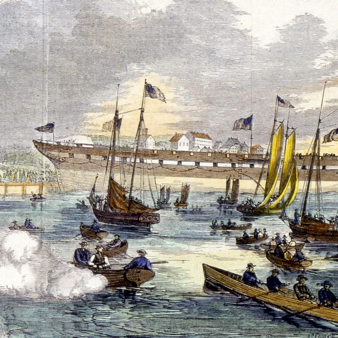 Hull of a ship launching into a harbor as crowds watch on piers and a swarm of boats. A cannon fires