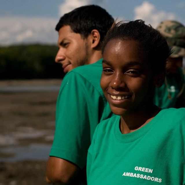 Close-up of a young woman in a green t-shirt standing with others on a beach. 