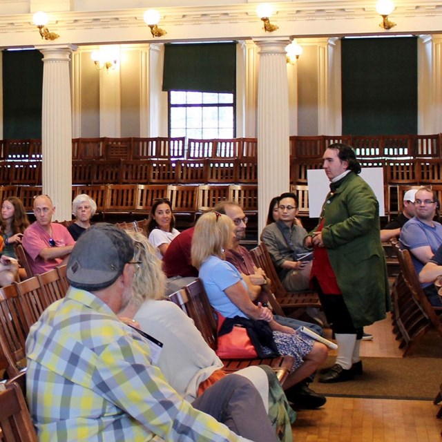 a person in the audience reads a quote as a ranger in period clothing watches on.