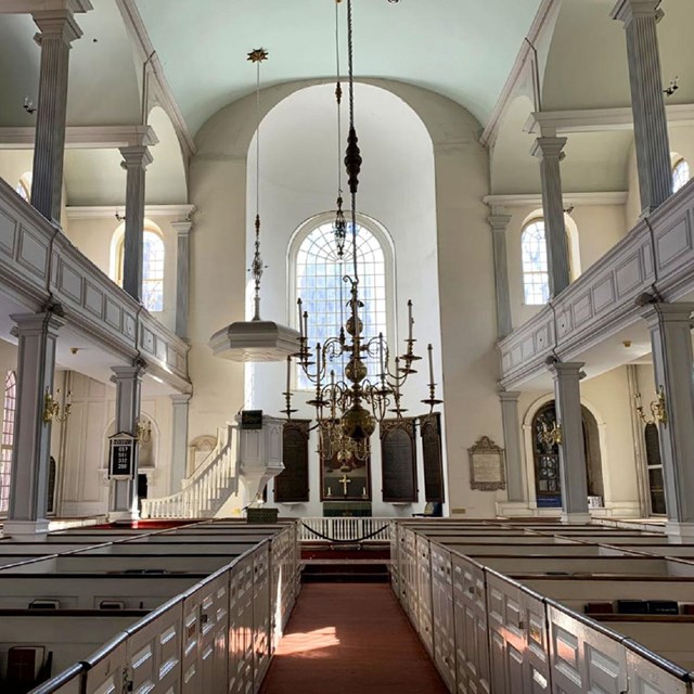 Interior of church looking down center aisle with white box pews on either side.