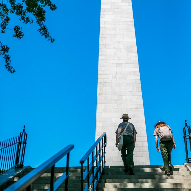 2 Rangers walking up a set of stairs to the Bunker Hill Monument. 