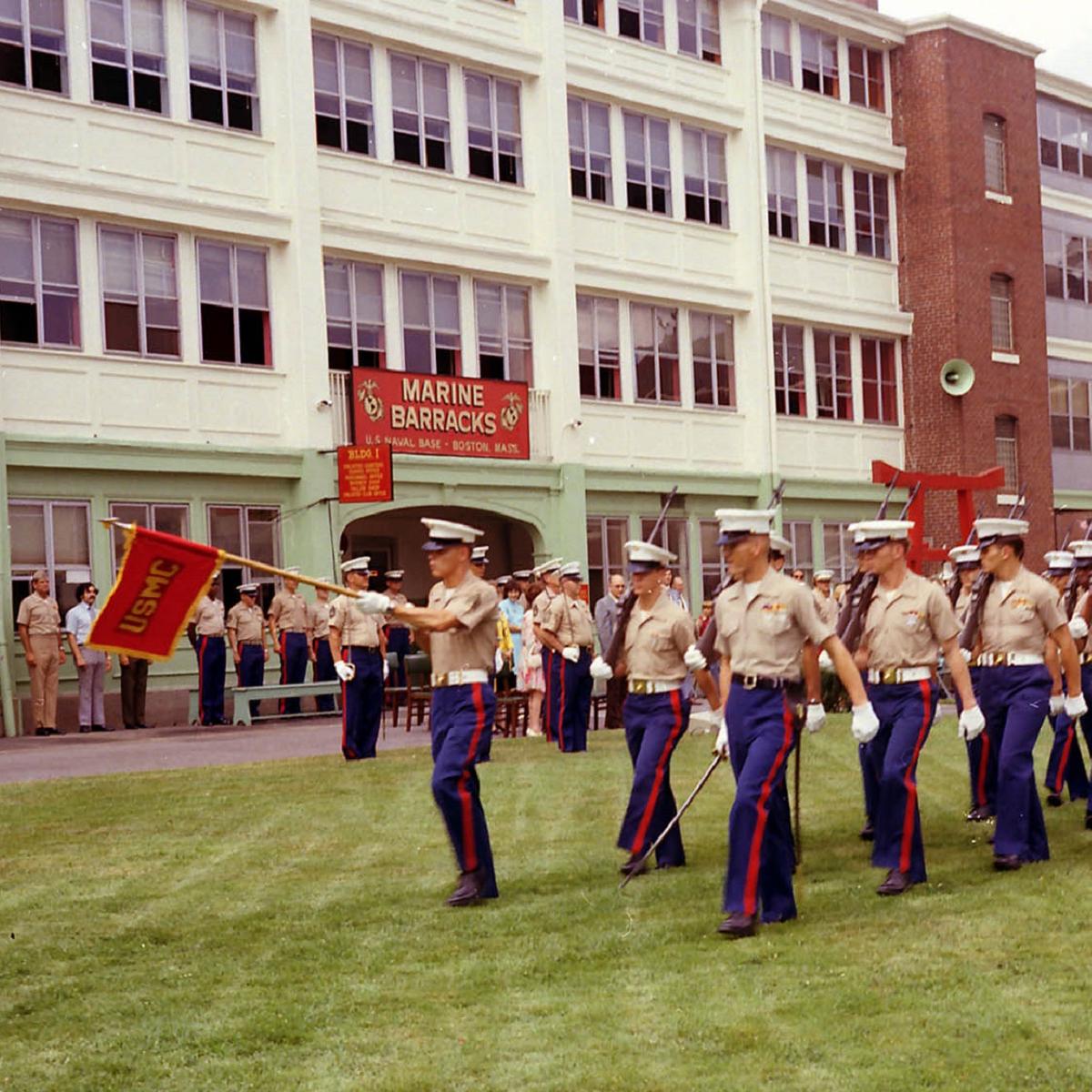 Marines in dress uniform marching on a lawn in front of the Marine Barracks, Charlestown Navy Yard.