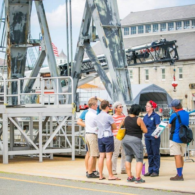 Ranger dressed as a Rosie the Riveter speaking with visitors at the Navy Yard.
